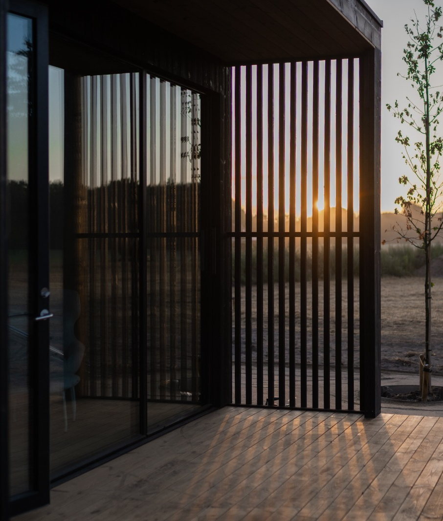 Leeg terras onder de overkapping van een eco lodge, met de avondzon door de houten lamellen