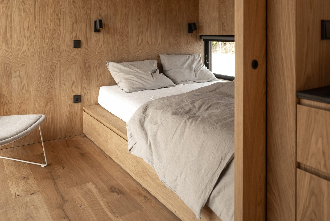 Slaapgedeelte met het bed op een houten verhoging en een raam bij het hoofdeinde